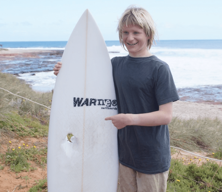 Un delfín salta sobre un joven surfista